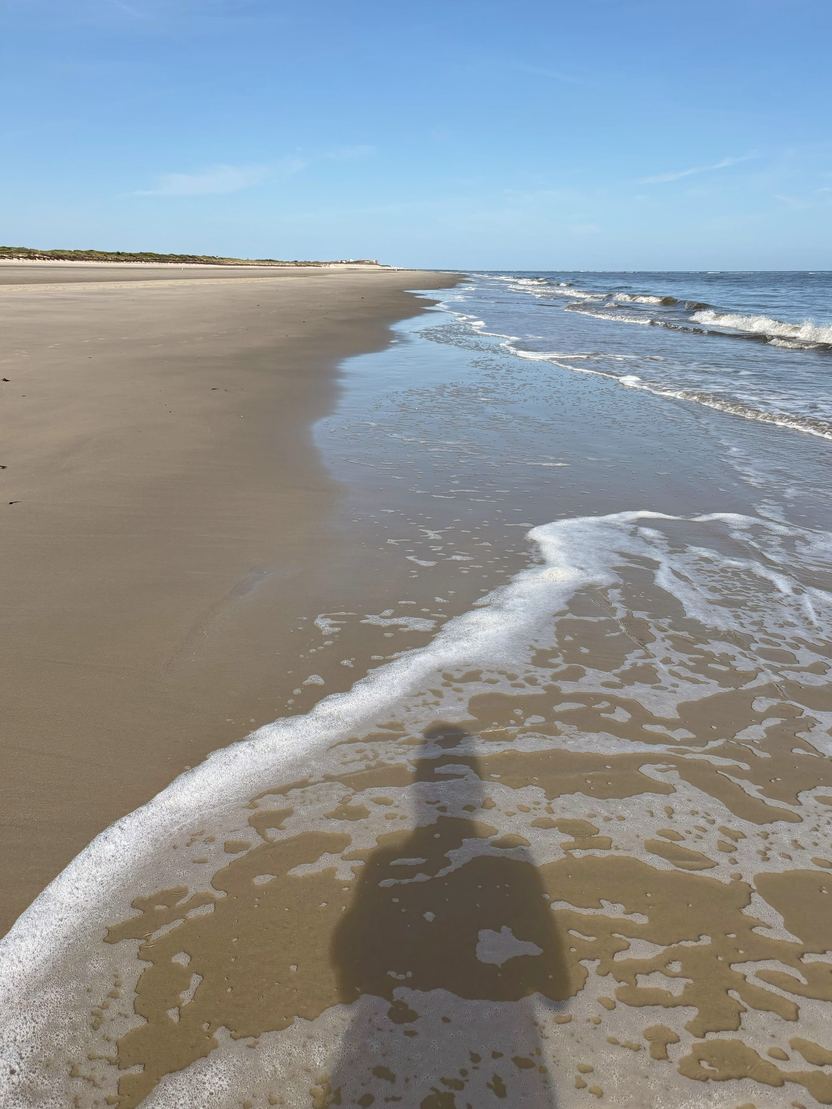 Schatten einer stehenden Person auf nassem Sand, berührt vom Meerschaum