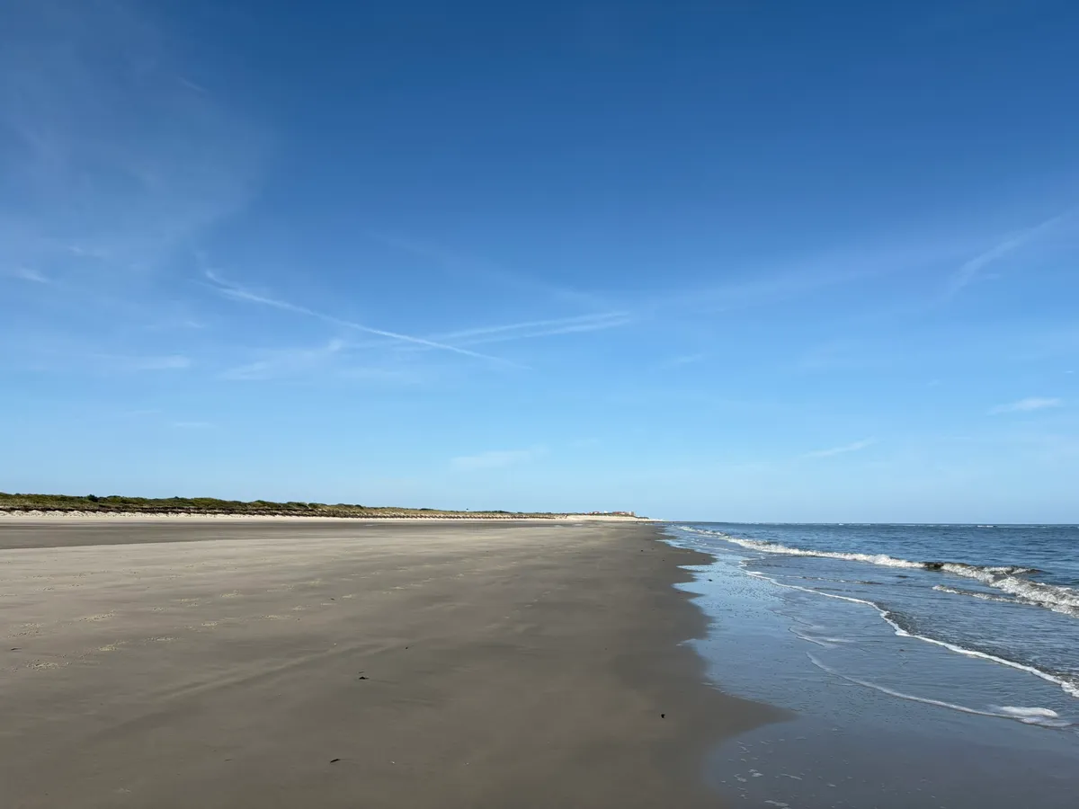 Weiter, leerer Sandstrand auf Wangerooge unter hellem Himmel, rechts das ruhige Meer